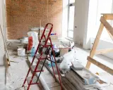 Remont w toku. Czym usunąć pył gipsowy? Na podłodze folia, drabina, wiadra, worki z materiałami budowlanymi i drewniane rusztowanie.